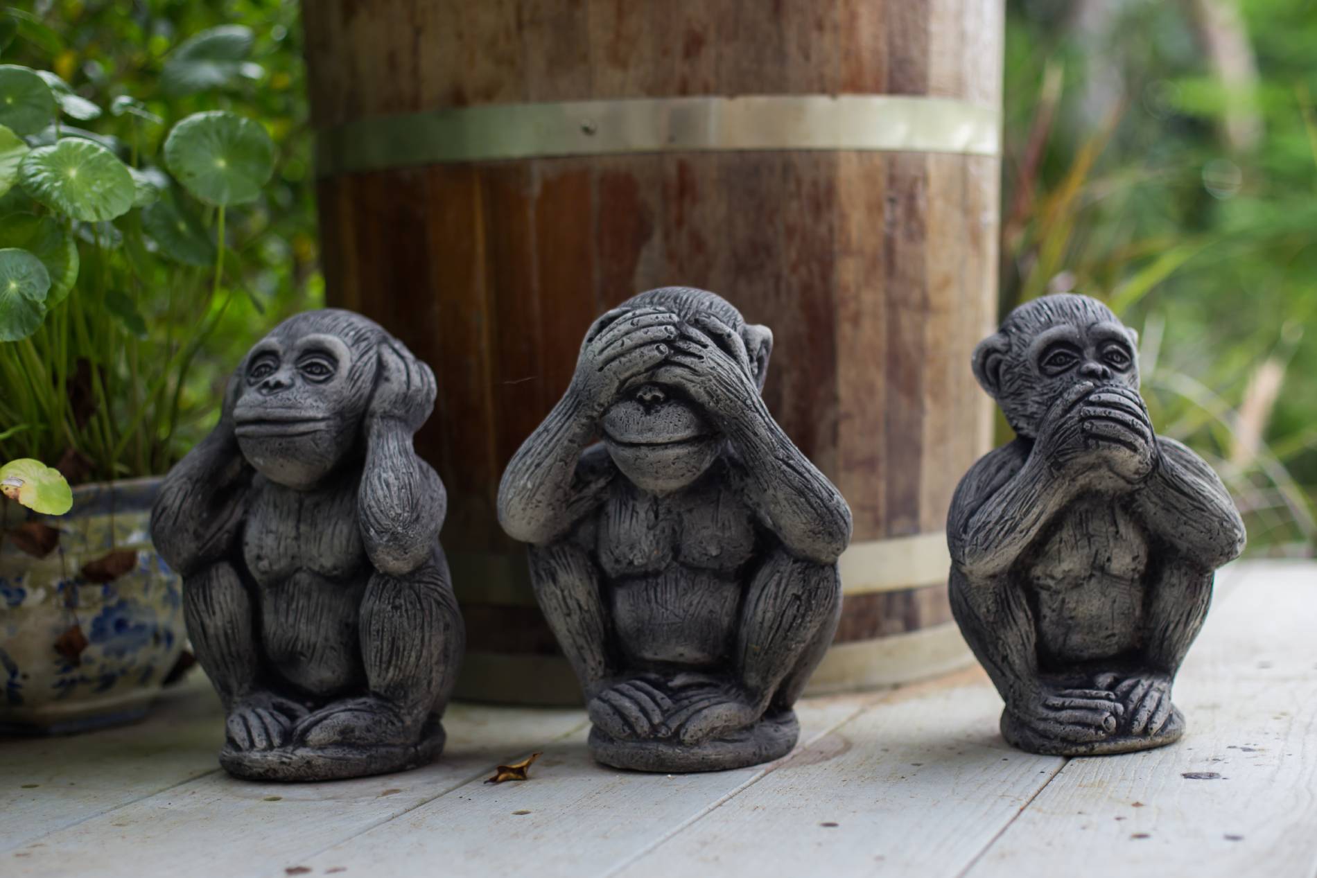Three stone see-no-evil, hear-no-evil, speak-no-evil monkeys beside a barrel